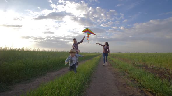 Joyful Childhood, Kid with Kite in Hands Runs Near Young Parents on Countryside During Recreation