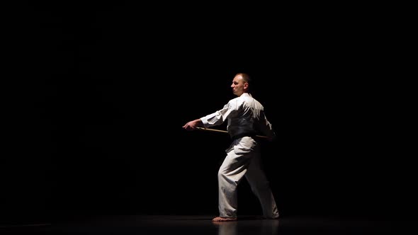 Kendo Fighter on White Kimono Practicing Martial Art with the Bamboo Bokken on Black Background.