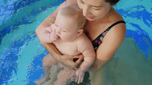 Happy Mother in Red Swimming Suit with Baby Son Surfing Water with Fun in Swimming Pool