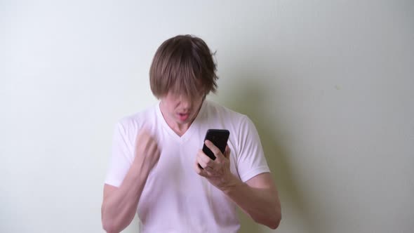 Happy Young Man with Long Hair Using Phone and Getting Good News