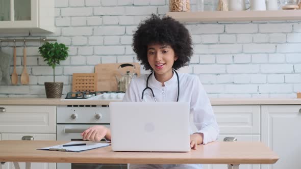 Afro American Woman Doctor in Robe Uses Laptop During Online Consultation at Home While Sitting at