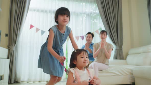 Asian young girl sibling have fun playing in living room with parent cheering and support in house.