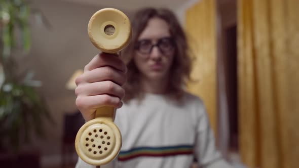 Closeup of Yellow Vintage Telephone Handset in Male Hand with Blurred 1980s 1990s Nerd at Background