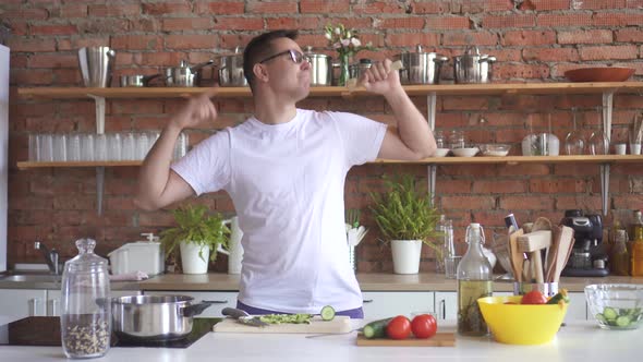 Portrait of a Young Man Dancing and Singing in the Kitchen He Cuts Vegetables