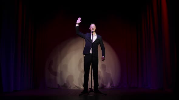 Man in Suit Stand Up Comedian Speaking Jokes in Micropphone Standing on Stage.