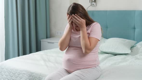 Sad Crying Pregnant Woman Suffering From Depression Sitting on Bed and Holding Her Head