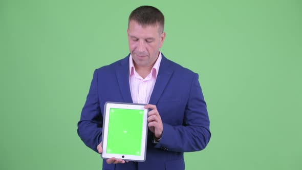 Mature Macho Businessman in Suit Thinking While Showing Digital Tablet