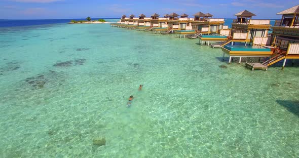 Aerial drone view of a man and woman couple with seascooters snorkeling near overwater bungalows