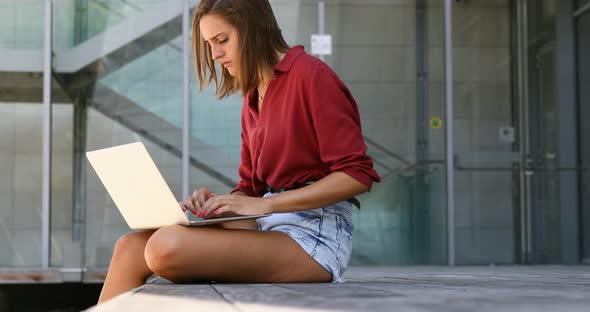 young woman writing outside on a laptop in shorts