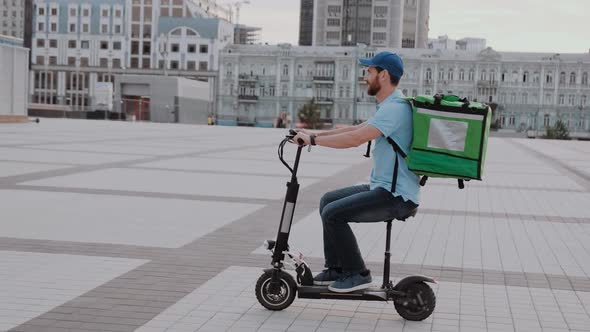 Man Courier Food Delivery with Thermal Backpack Rides the Street on an Electric Scooter Deliver