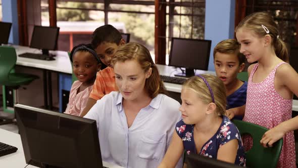 Teacher assisting school kids on personal computer in classroom