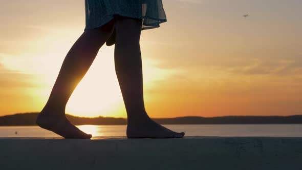 Close Up Of Women Feet Are On The Beach In The Flicker Rays Of The Sunset