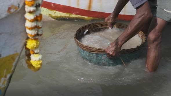 Indian fisherman rinsing his catch of fish and prawns in a woven basket  sea water slow motion