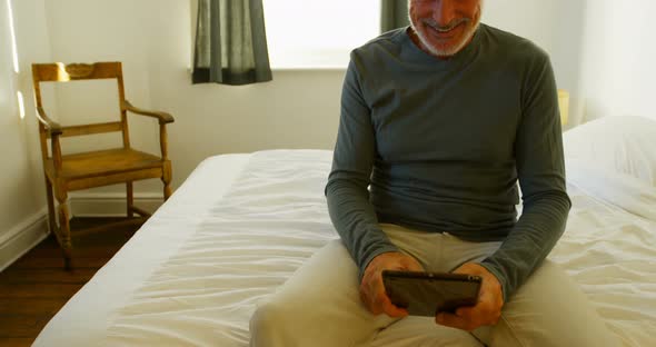 Senior man using digital tablet on bed in bedroom 4k