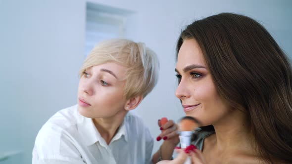 Blonde Makeup Artist Doing Professional Makeup for Brunette Model