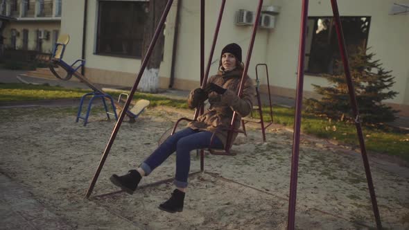 Young Attractive Redhaired Woman Swinging on a Swing in the City at Sunset or Sunrise