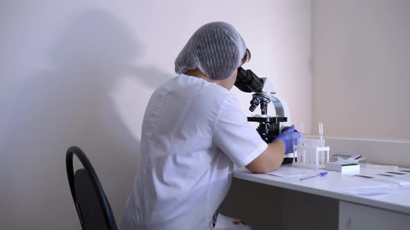 Woman Scientist in Lab Conducts Research Studying Specimen Under Microscope