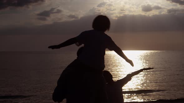 Silhouette of Happy asian family looking sunset and stretch the arms same plane on the beach.