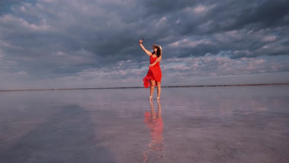 Young Woman Takes a Selfie While Standing on the Shore of a Pink Lake in Which the Sky Is Reflected