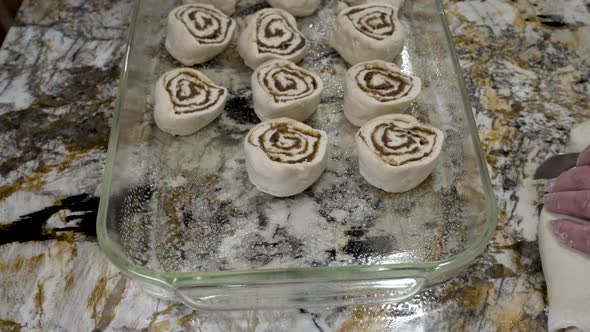 Placing raw cinnamon rolls in a pan so the dough can raise before baking