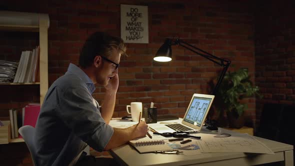 Young Successful Designer with Light Beard and Blue Shirt Gladly Talking on Mobile Phone with Client