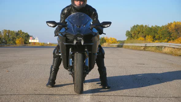 Front View of Young Biker in Helmet and Leather Jacket is Sitting on Motorcycle at Highway Road and