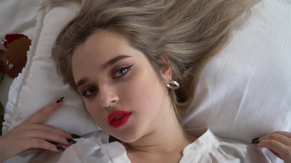 Portrait of Young Lady with Bright Makeup and Pierced Nose Is Lying on the Bed Close Up