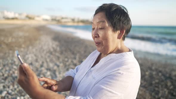 Positive Old Asian Woman Talking in Slow Motion Using Video Chat on Smartphone Bragging Vacations on