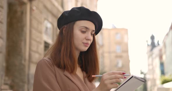 Girl Artist with a Notebook Looks Into the Distance on the Street