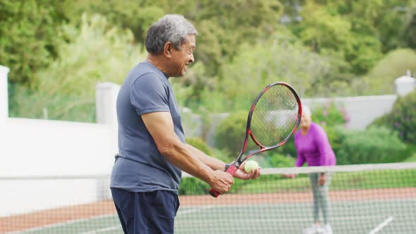 Video of happy biracial senior man holding racket and starting match on tennis court