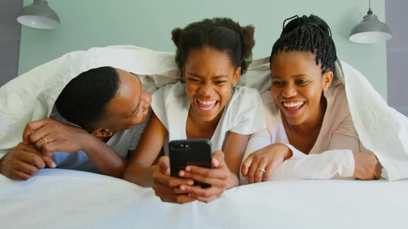 Front view of happy black family using mobile phone on bed in a comfortable home 4k