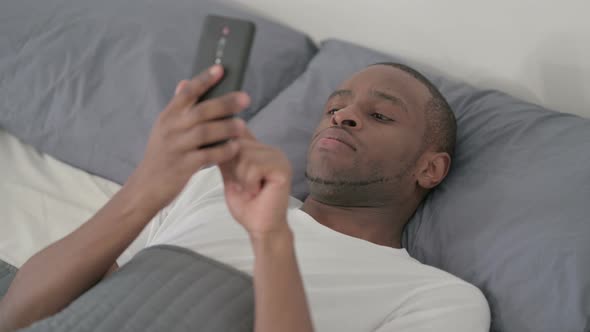 African Man Using Smartphone While Sleeping in Bed Close Up