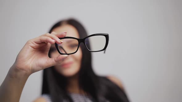 Pretty woman shows from left to right stylish eyeglasses and puts them on