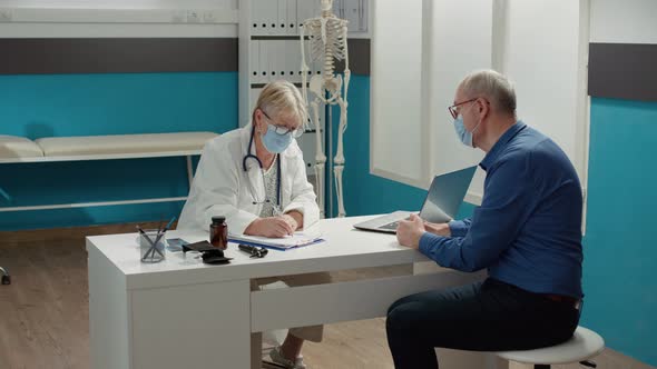 Health Specialist Taking Notes at Consultation Appointment with Old Man