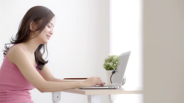 Beautiful young freelance asian woman smiling working and typing on laptop computer.