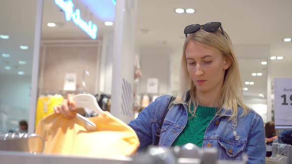 Beautiful woman chooses and buys clothes in shopping mall