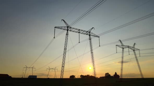 Dark Silhouette of High Voltage Towers with Electric Power Lines at Sunrise