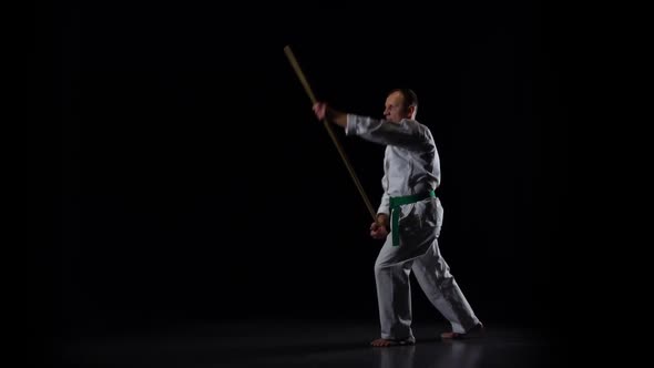 Kendo Fighter on White Kimono Practicing Martial Art with the Bamboo Bokken on Black Background