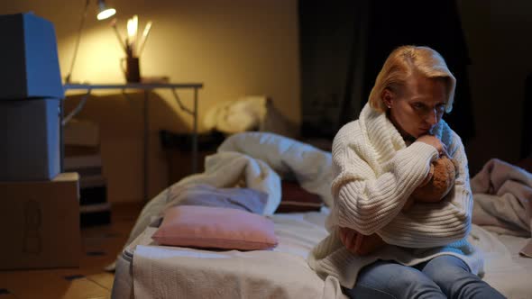 Hopeless Devastated Ukrainian Woman Hugging Teddy Bear Sitting on the Right in Bomb Shelter