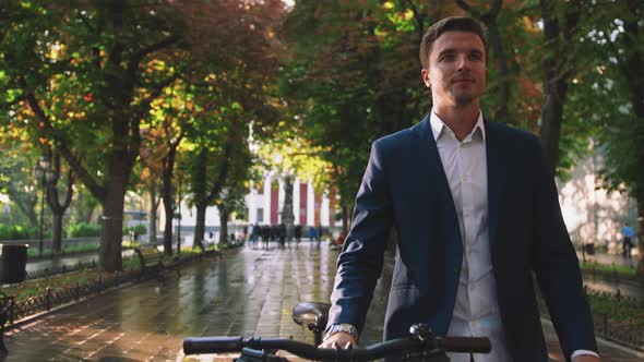 Handsome Young Man Walking with His Bicycle in Park in City Center During Sunrise