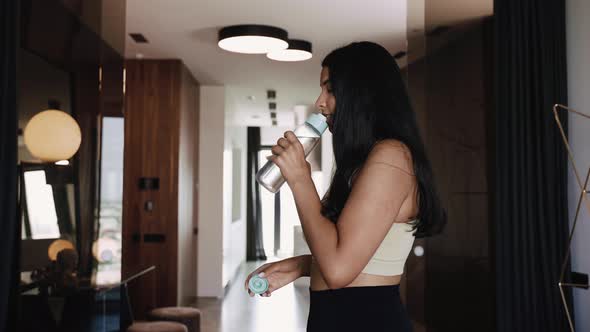 Young Darkskinned Brunette Drinks Water From a Bottle in Beautiful Interior