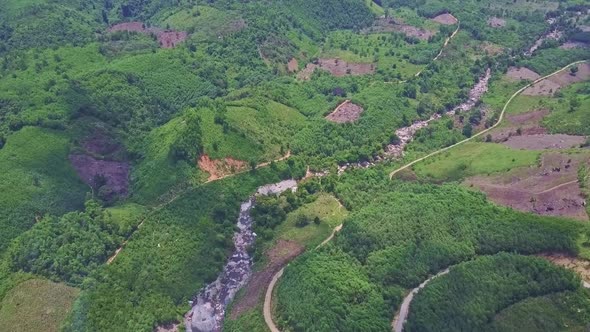 Drone Flies Above Long Creek Running Among Wild Hilly Jungles