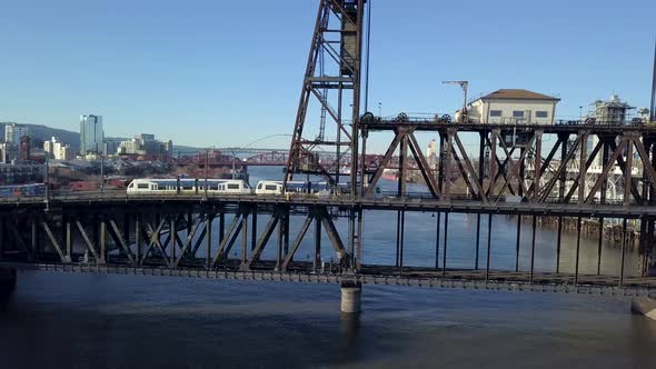 Aerial follow of a light rail train crossing a bridge over the river in the city.