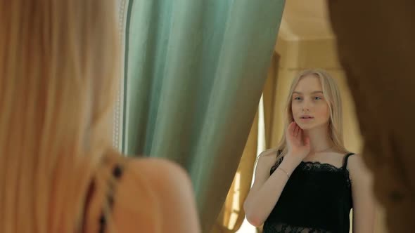 Young woman with blue eyes and blonde hair looking at her reflection in mirror