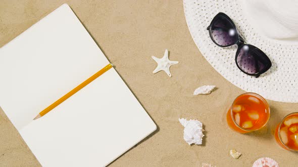 Notebook, Cocktails, Hat and Shades on Beach Sand