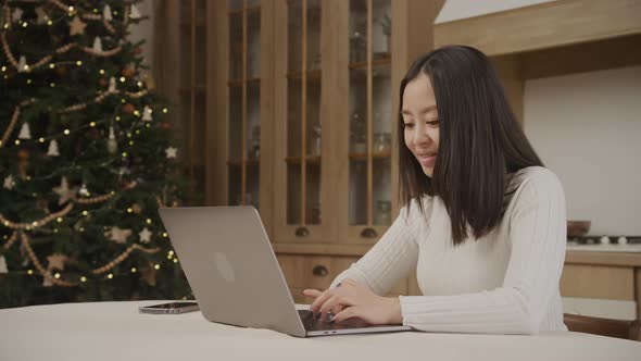 Asian Woman Browsing Online on a Laptop Computer with a Christmas Tree Background