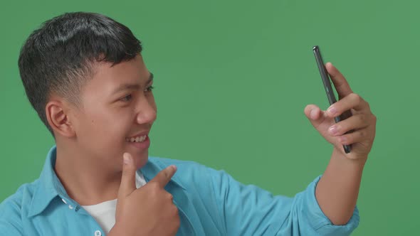 The Smiling Young Asian Boy Making Selfie While Standing On Green Screen In The Studio