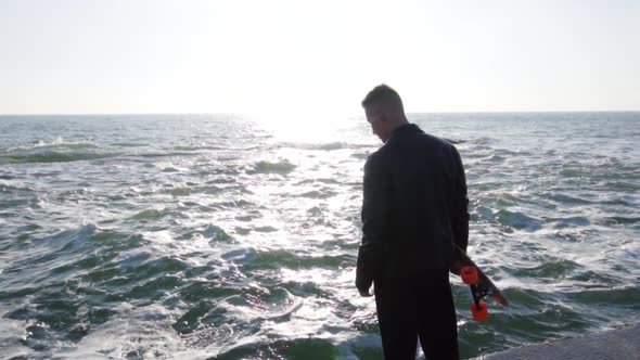 Young Man Holds His Longboard Standing By the Sea