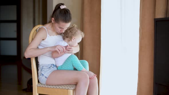 A young mother takes care of the nails of a little restless daughter