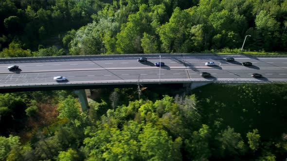 Convoy of vehicles in pursuit over highway bridge through lush green forested landscape, fast tracki